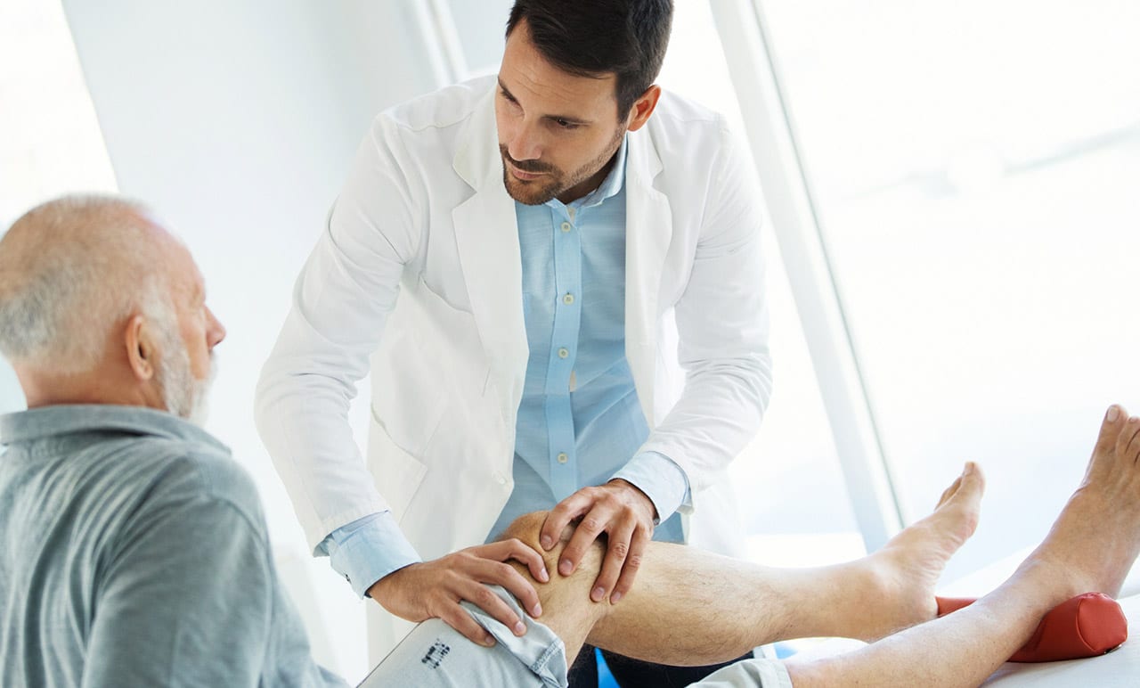 Male-doctor-examining-male-patient’s-knee-for-signs-of-knee-osteoarthritis